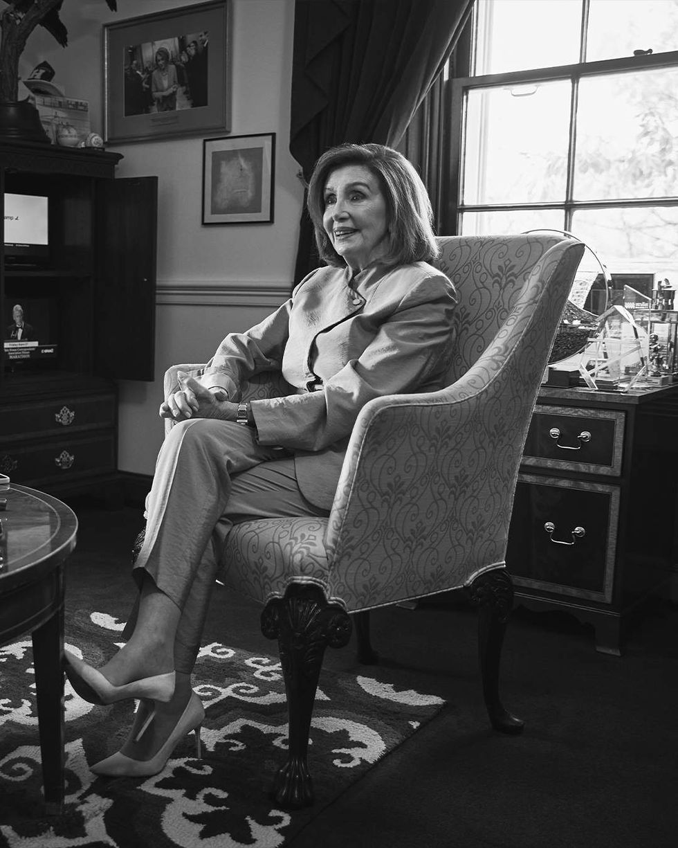 A black and white image of Nancy Pelosi sitting in a chair in her office, photographed for The Advocate.