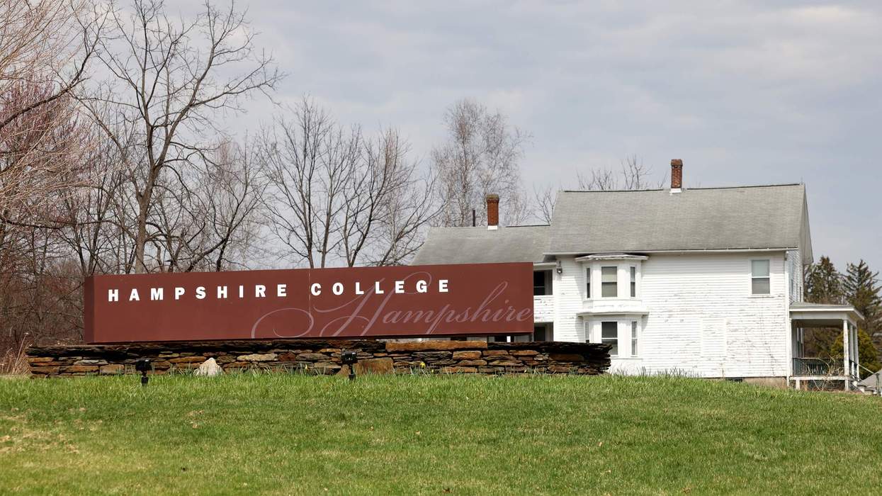 A brown and white sign on a grassy hill beside some woodlands and a white house reads: "Hampshire College."