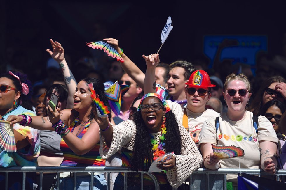 a crowd cheers and wears rainbow clothing and accessories at the worldpride parade