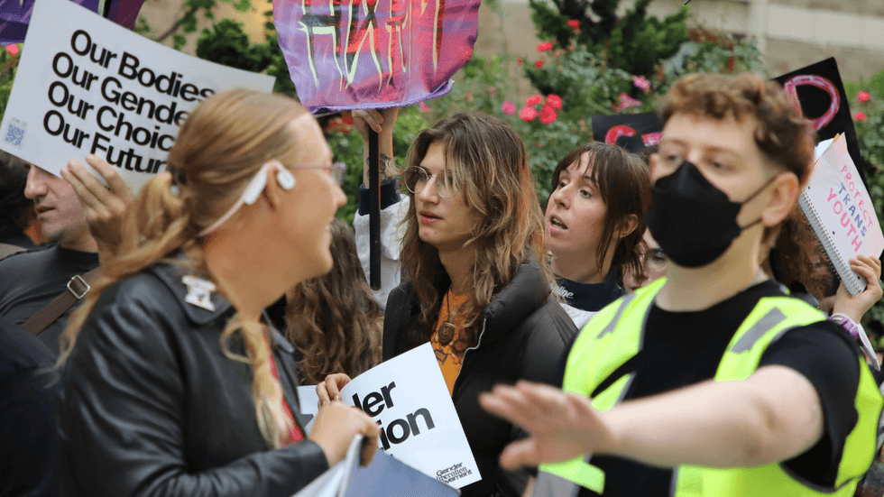 A crowd of people marches with colorful pro-trans rights signs.