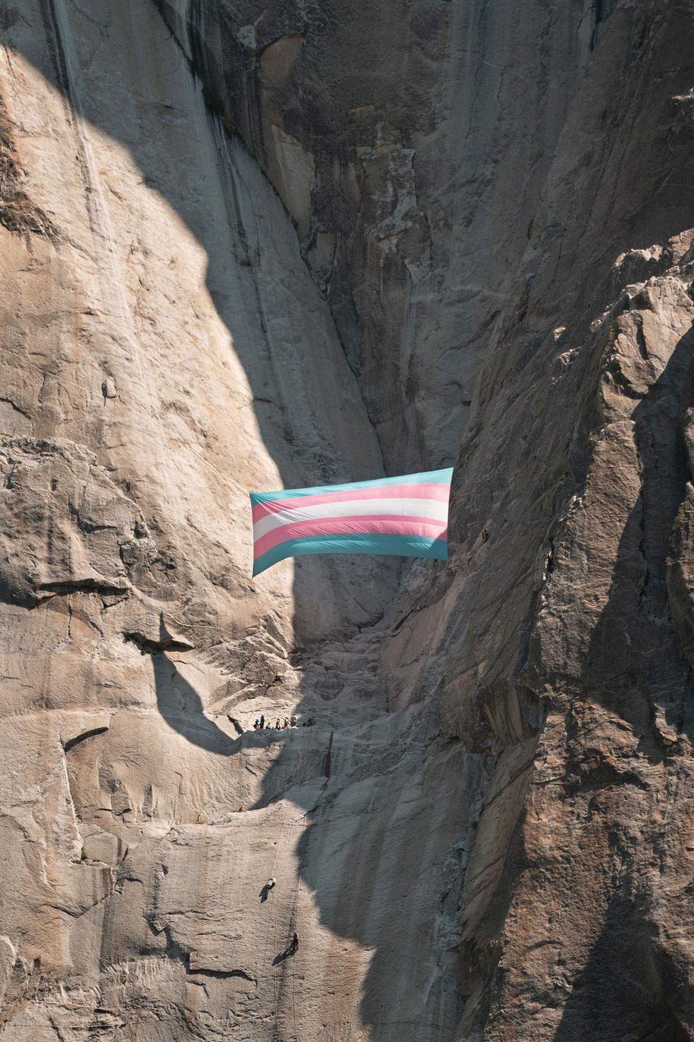 a giant trans pride flag hanging off a cliff in in Yosemite