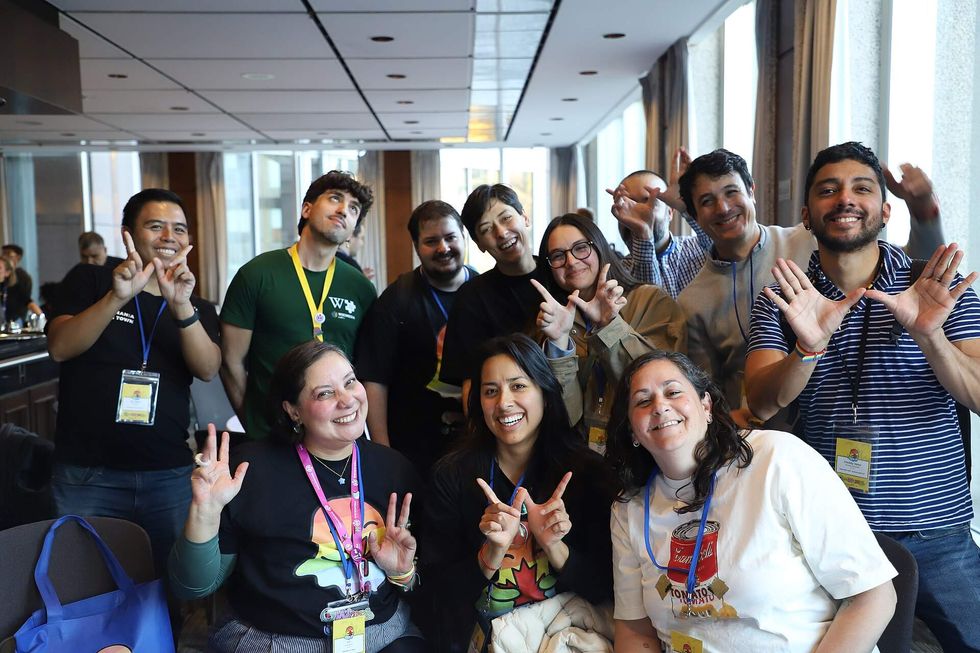 A group of people making "W" shapes with their fingers gather together and smile toward the camera.