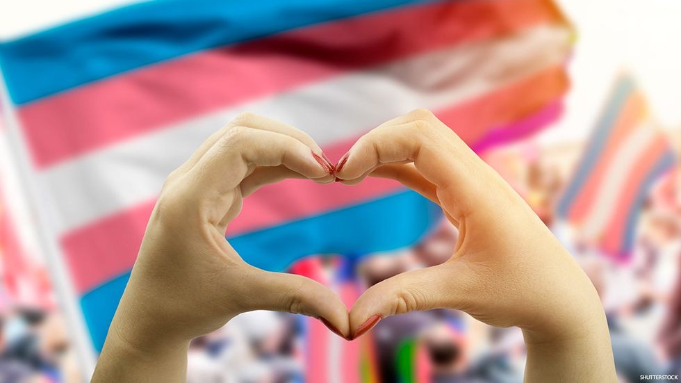 A hand heart in front of a trans pride flag