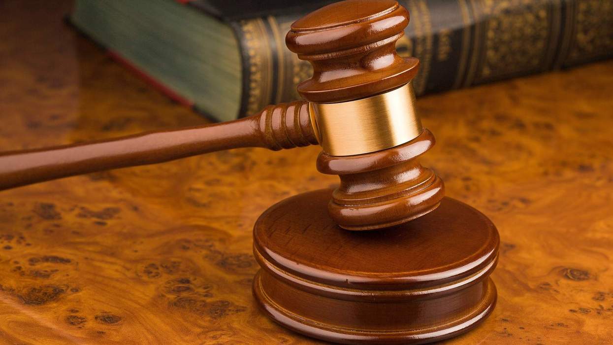 A judge's gavel rests atop a wooden block on a marble desk. A book sits behind it.