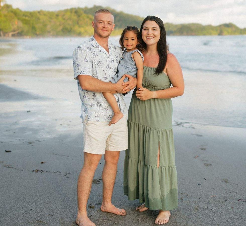 a man holding his young daughter standing next to his wife standing on the beach