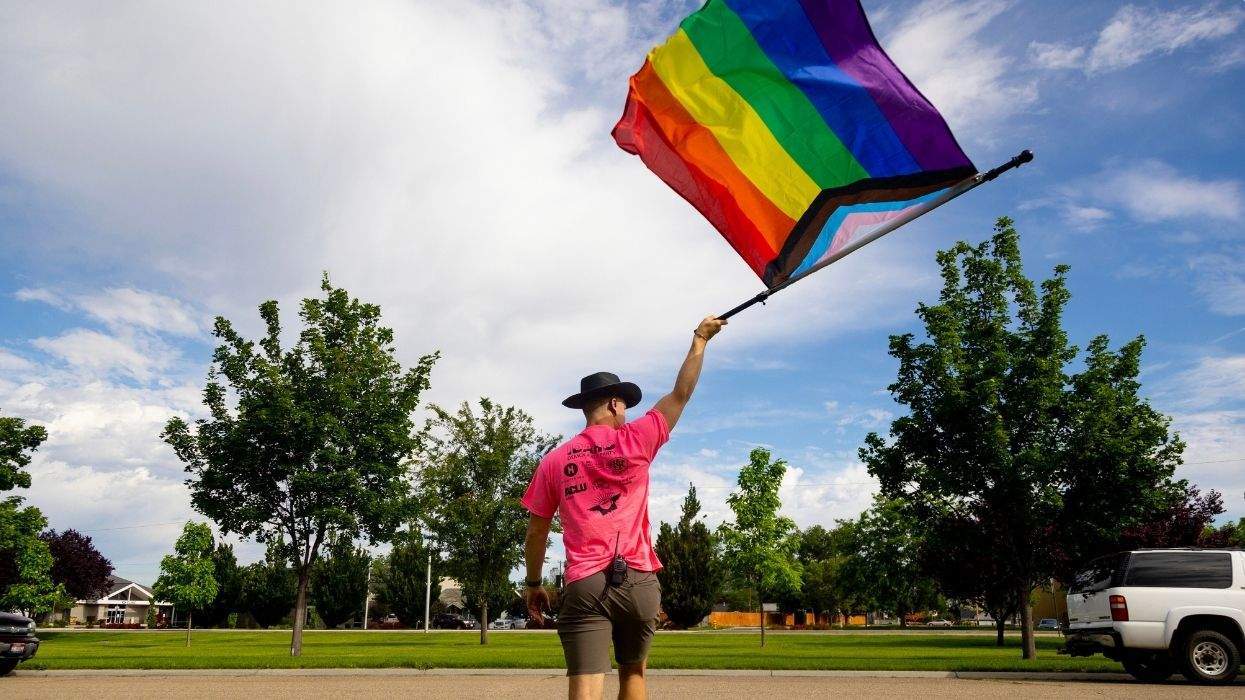 a man walks across the street with a pride flag waving overhead