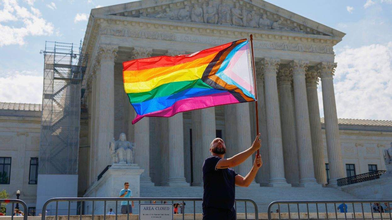 A man waves the progress pride flag in front of the Supreme Court building