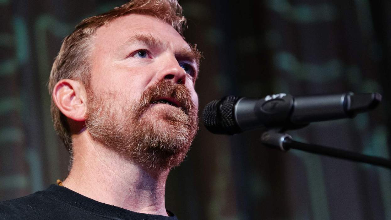 A man with red hair and a beard speaks into a microphone.