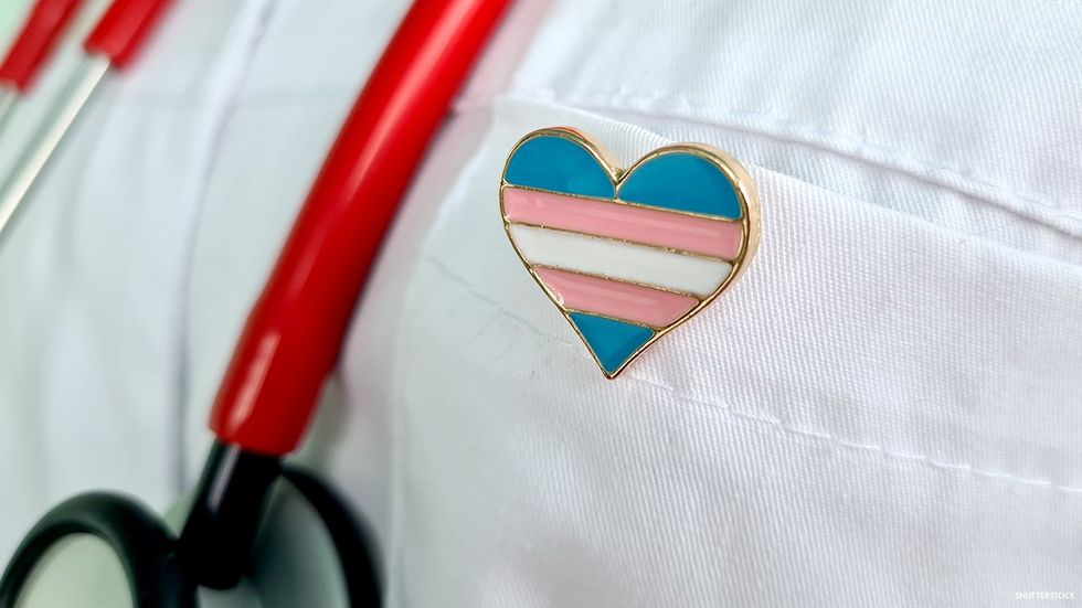 A medical provider wearing a stethoscope and a transgender flag heart pin.