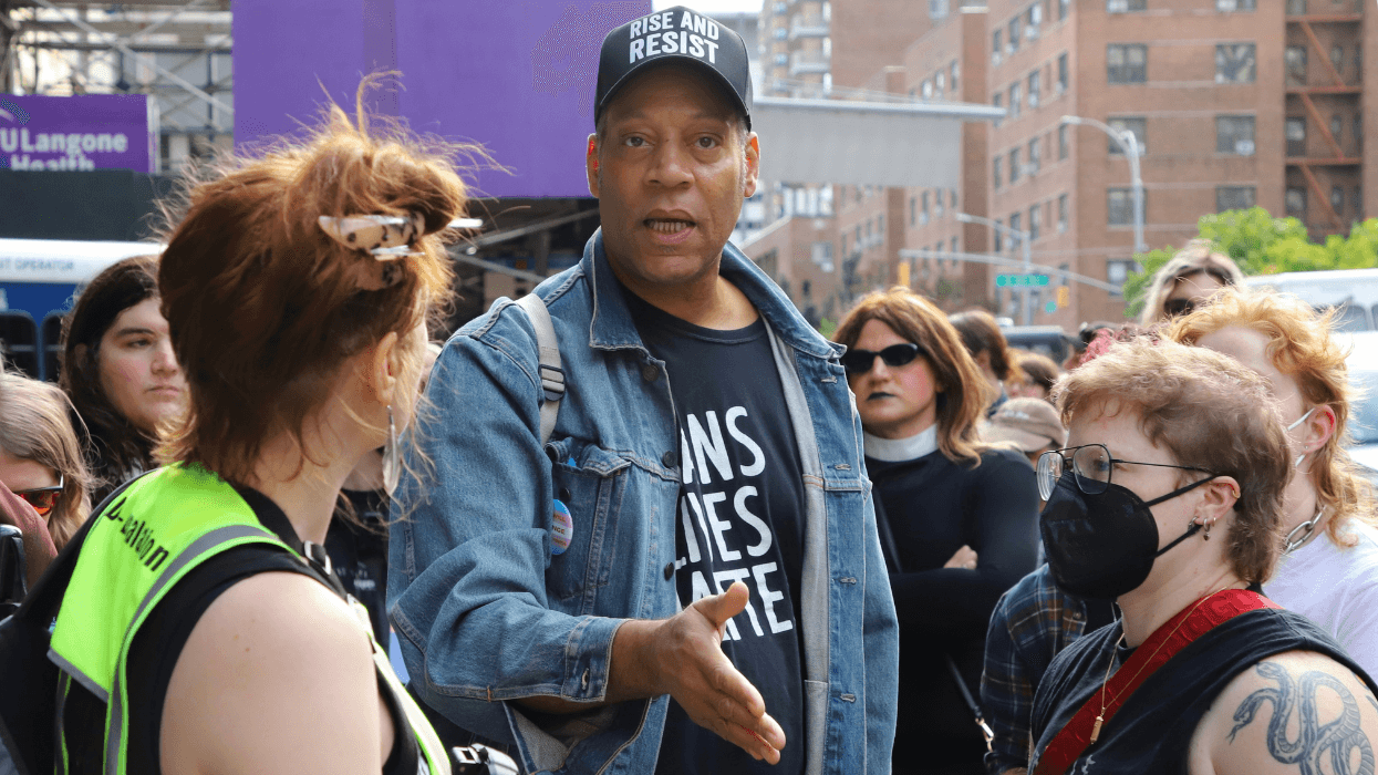 A person in a hat that says "Rise and resist" gestures at a crowd at a protest.