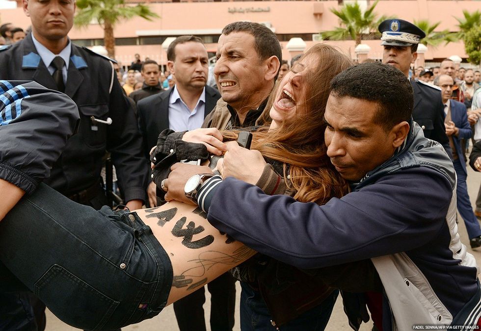 A person with writing on their torso is carried away from a protest by authorities.
