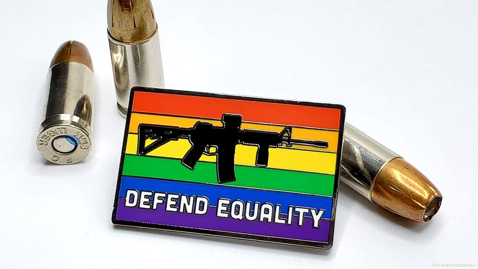 A pride flag pin with an AR-15 style rifle on it and bullets in the background of the overall image.