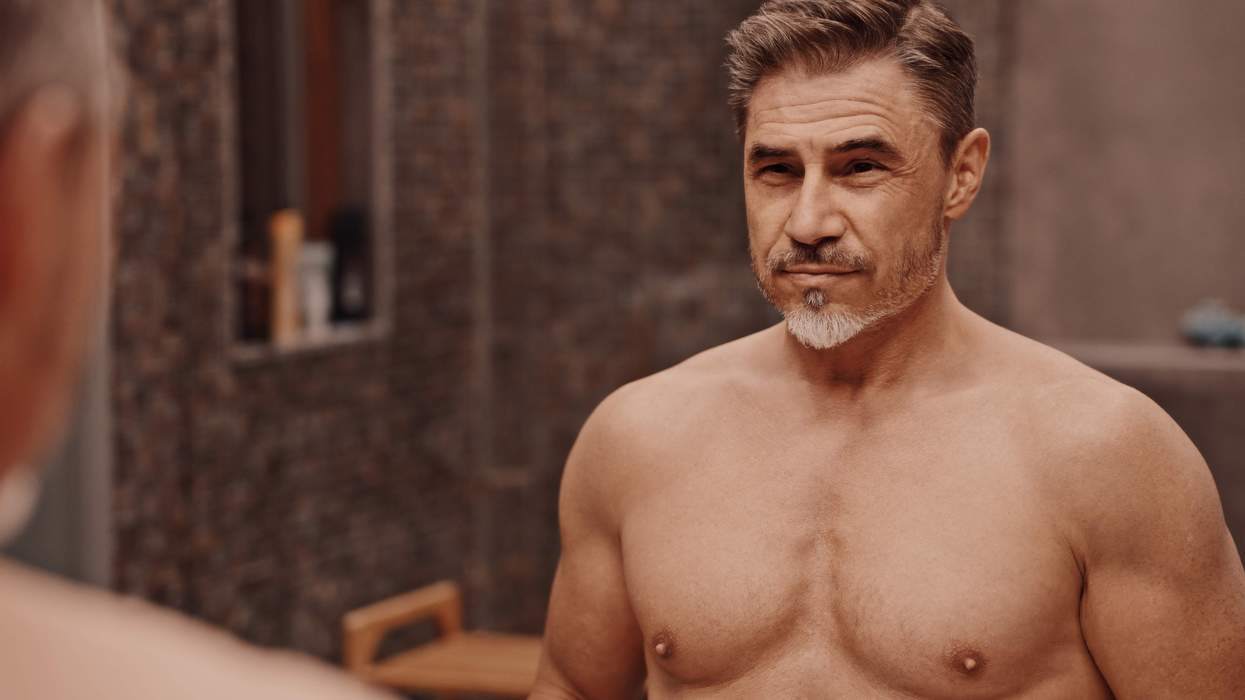 A shirtless older man looking in the mirror.