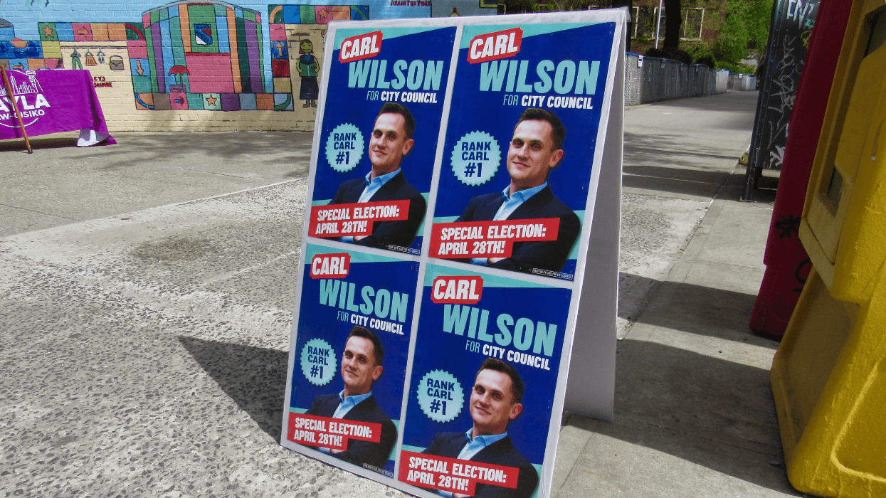 A sign standing on the sidewalk reads "Carl Wilson for the City Council."