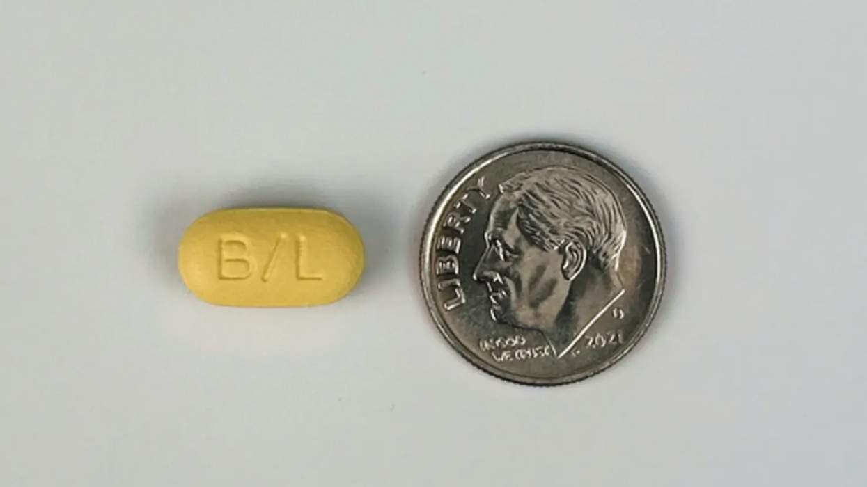 a small yellow pill with a B and L on it sitting next to a dime