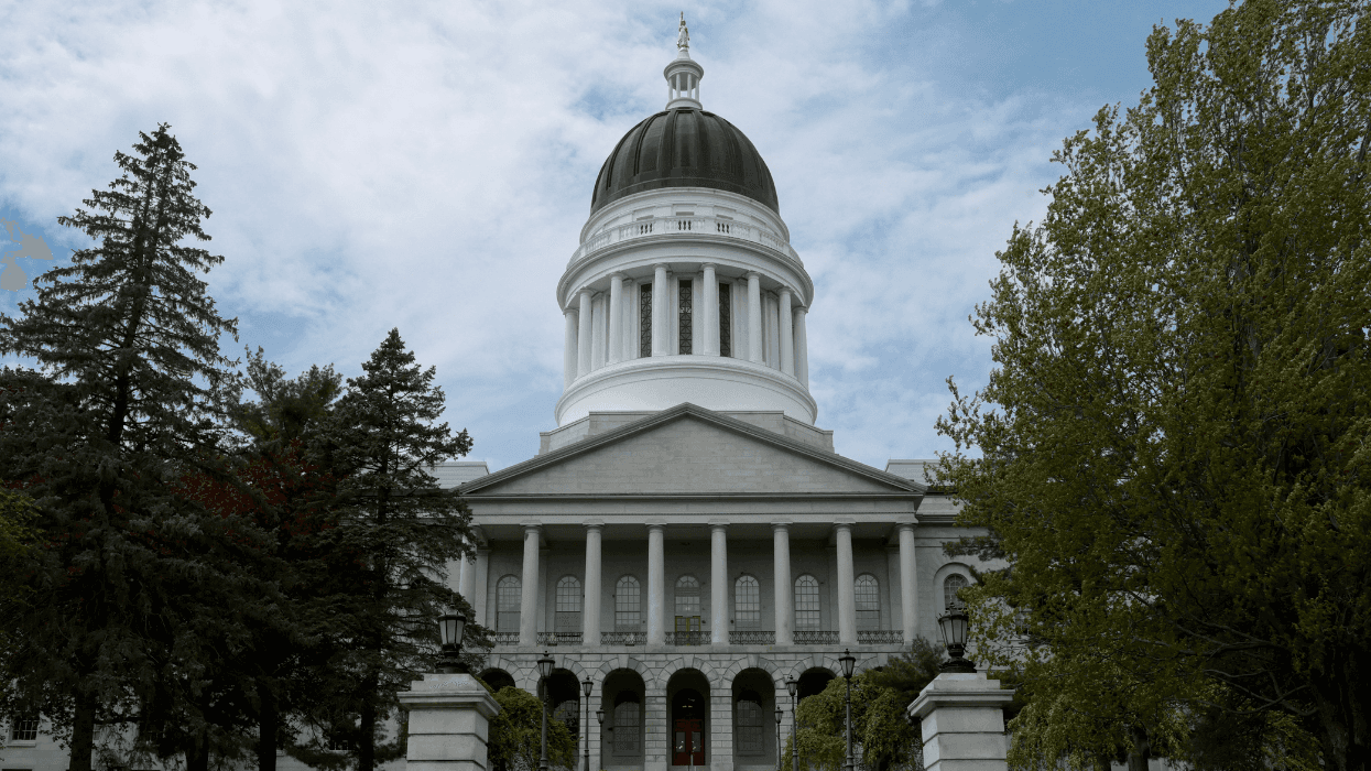 A statehouse with a black dome and gold figure on top. Trees lead up to its entryway, which has several columns and arches.