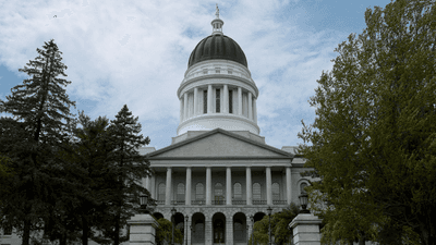 A statehouse with a black dome and gold figure on top. Trees lead up to its entryway, which has several columns and arches.