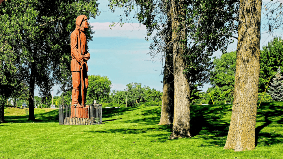 A statue of a person with a rifle stands tall at the end of a lush green field.