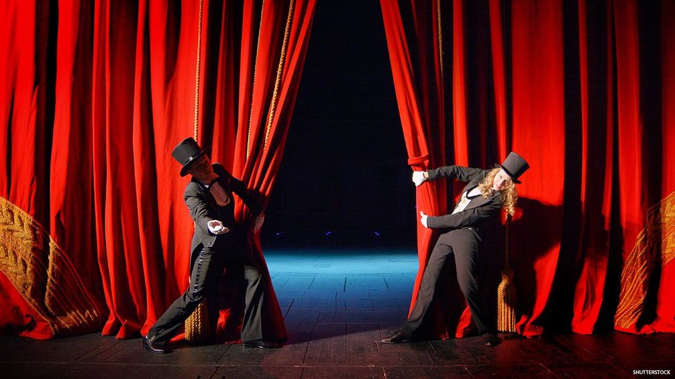 A theatre stage with two people in top hats holding the curtain.