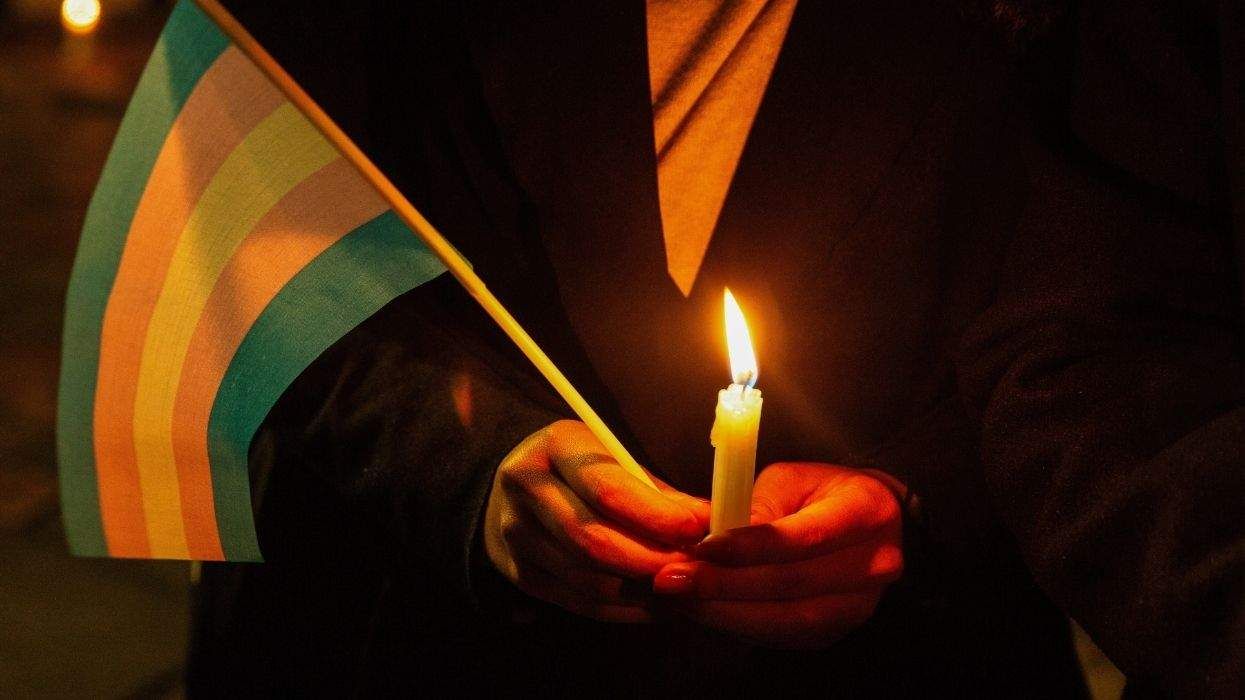 A trans pride flag and a candle held in clasped hands
