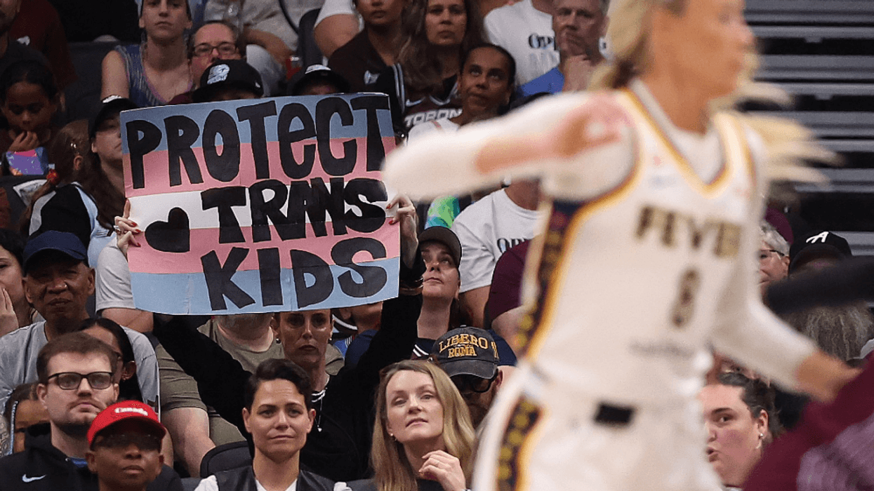 a WNBA fan holds a Protect Trans Kids sign as Sophie Cunningham plays
