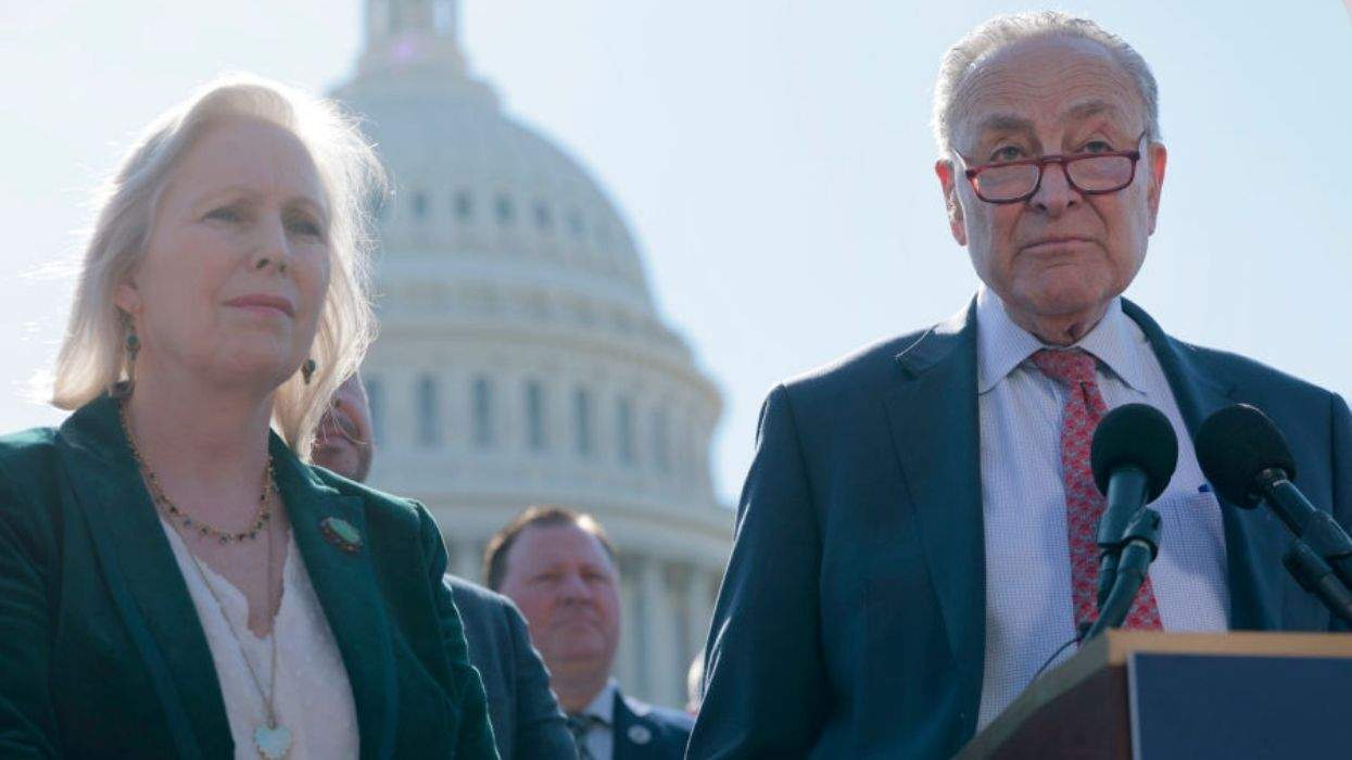 A woman and man in formal attire stand at a podium with microphones and look forward. They are outside the U.S. Capitol, with the building's rotunda clearly visible in the sky behind them.