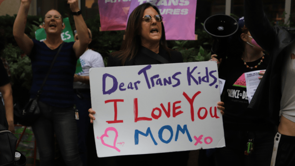 A woman holds a hand-made sign that reads: "Dear Trans Kids, I love you. XO Mom."