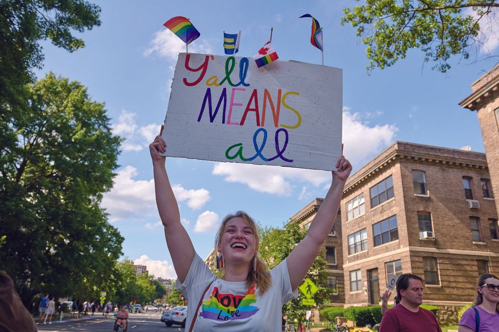 a woman holds a sign that says y'all mean all at the 2025 worldpride parade in washington dc