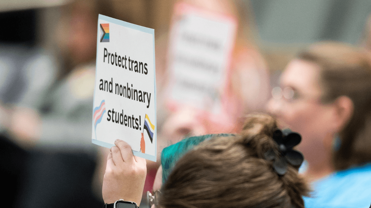 A woman holds up a sign that reads "Protect trans and nonbinary students!" at a school board meeting.