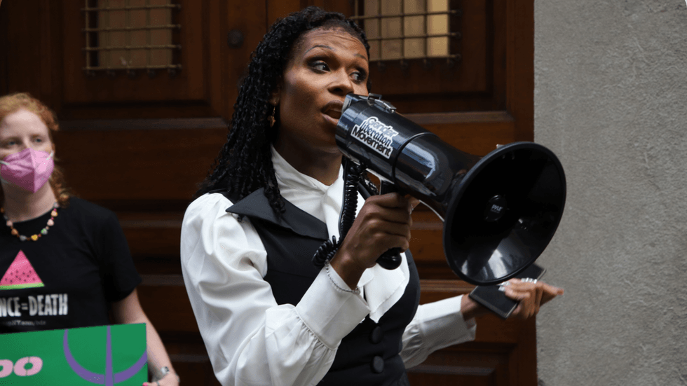 A woman speaks into a black megaphone with a sticker that reads "Gender Liberation Movement."