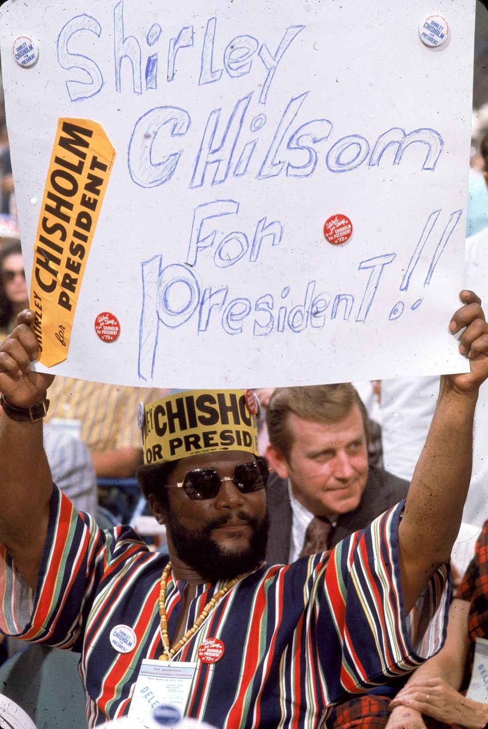 African American delegate stands on the floor of the Democratic National Convention holding a sign reading Shirley Chisholm for President Miami Beach Florida 1972
