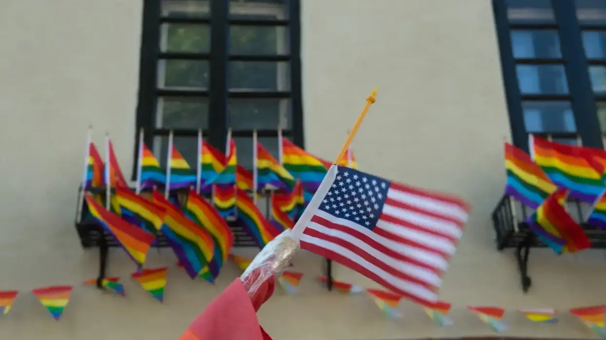 An American flag waves in front of a building decorated with multiple rainbow Pride flags