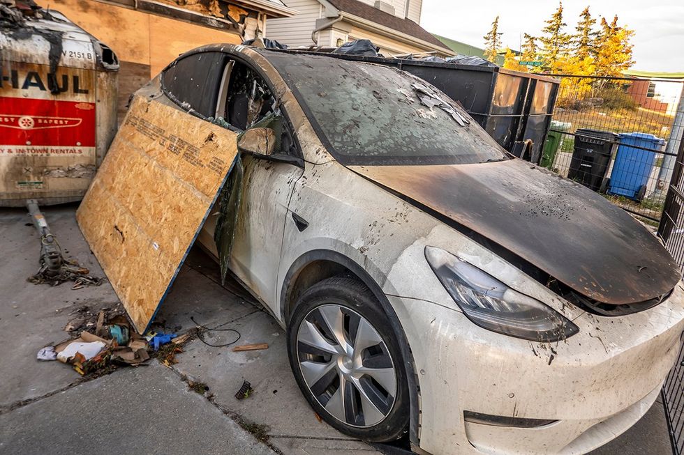 An electric Tesla car with fire damage in a front house driveway.