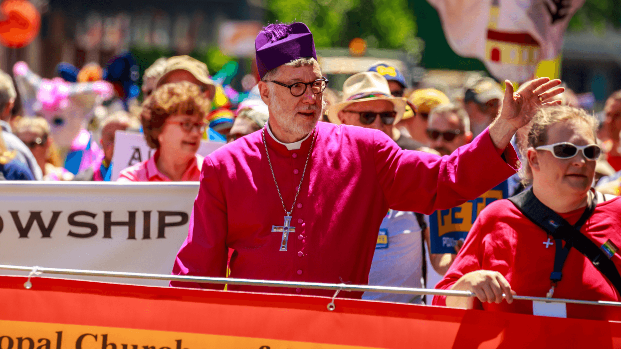An Episcopal bishop and other church members march in a Pride parade carrying a rainbow banner