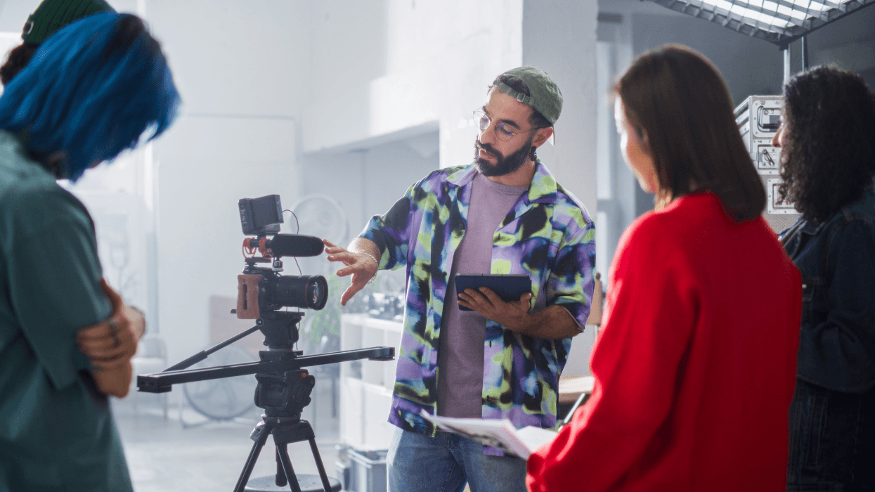 An instructor demonstrates a video camera setup to a small group of students during a documentary filmmaking workshop