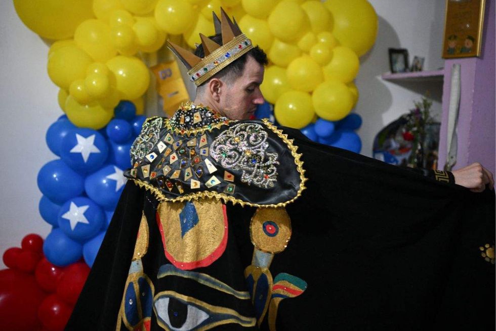 andry hernandez romero wearing a black cape adorned with images and a crown