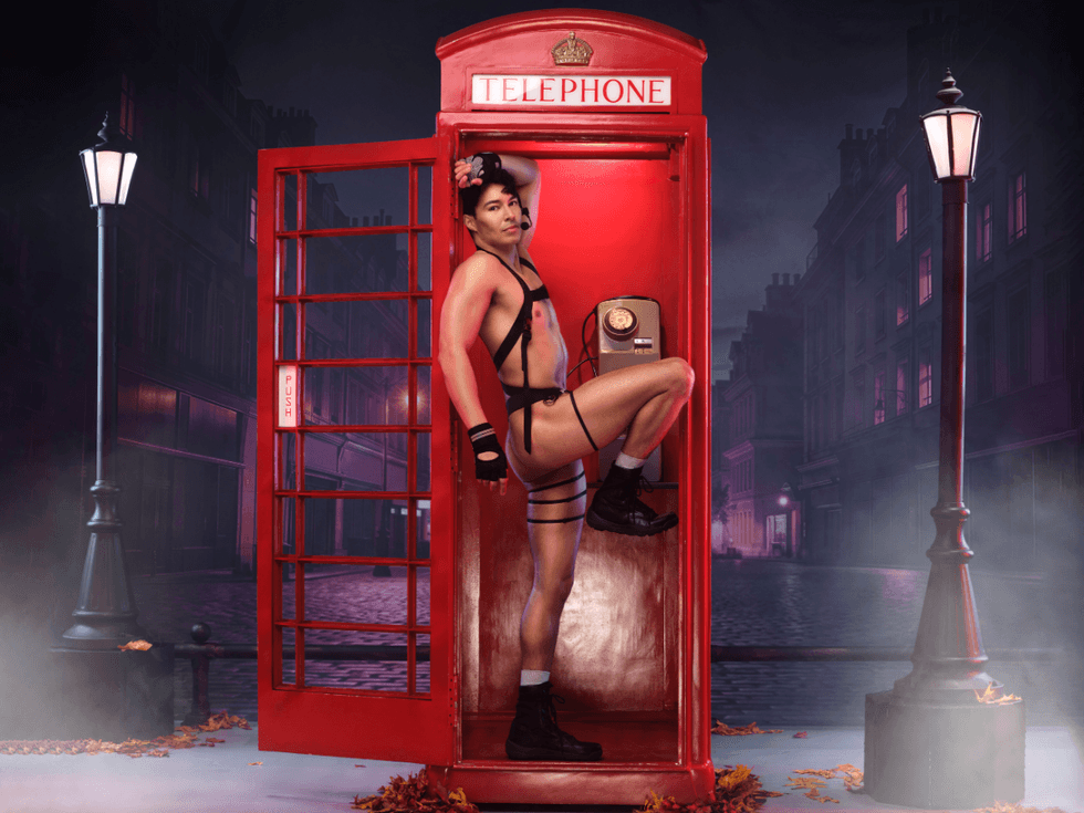 Anthony Sanchez, dressed as Ethan Hunt, stands in front of a red telephone box in London, wearing an open white shirt and black harness, on a spooky night street