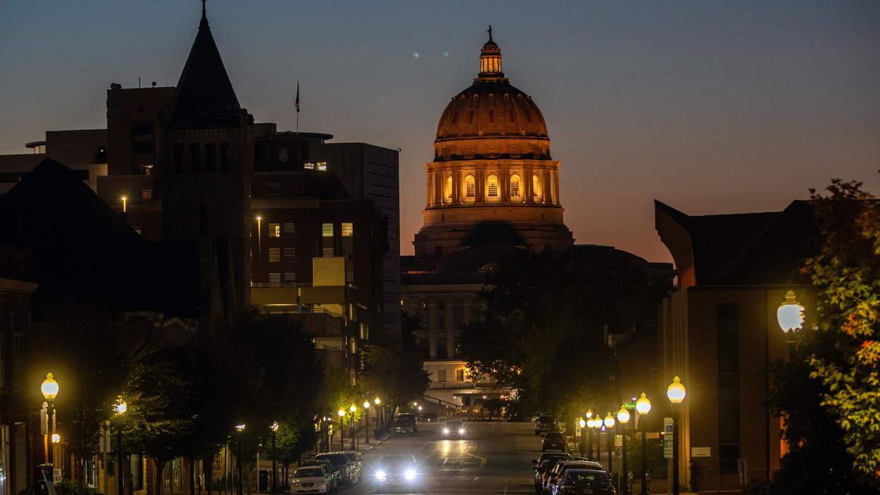 At the end of a city street with lamp posts lit at dusk, the dome of the Missouri statehouse is lit up with yellow lights.