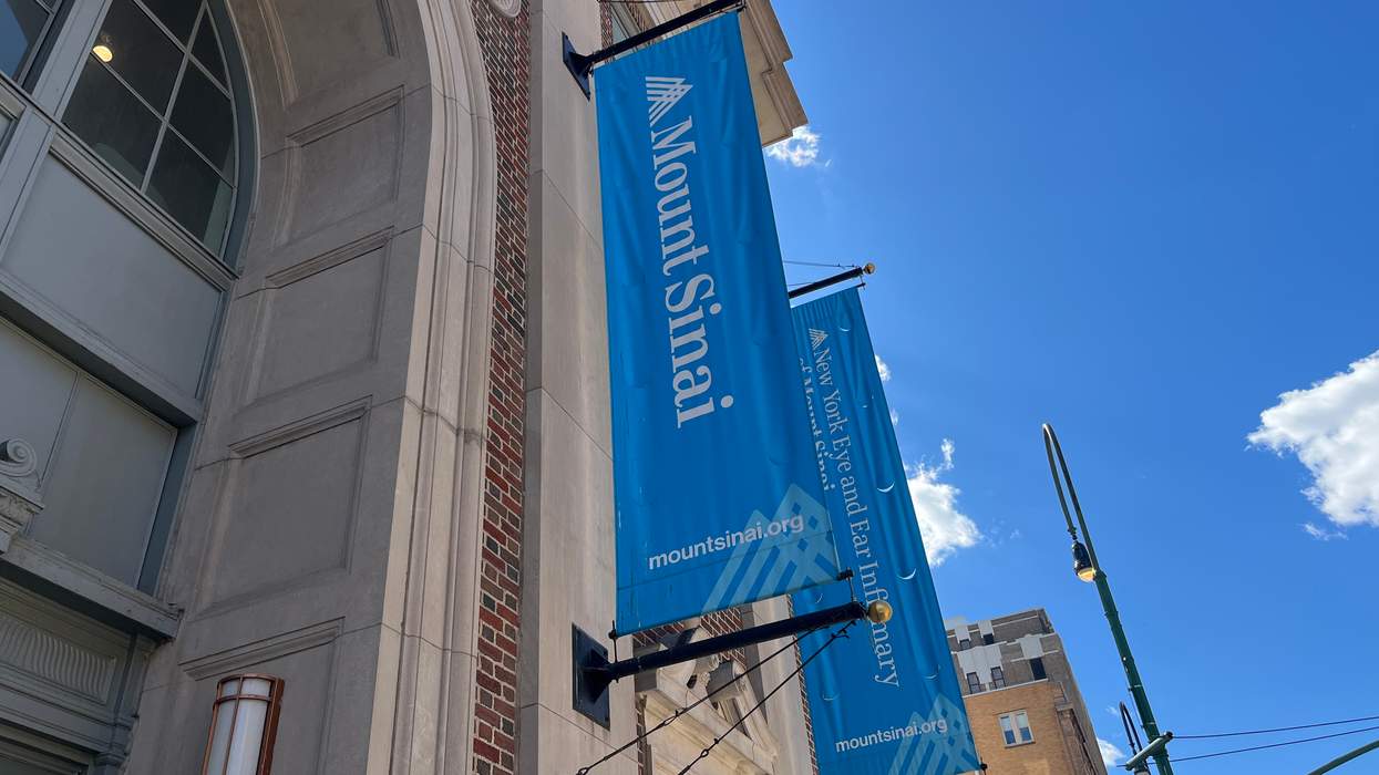 Blue banners that read "Mount Sinai" hang from the side of a red brick building on a city street.