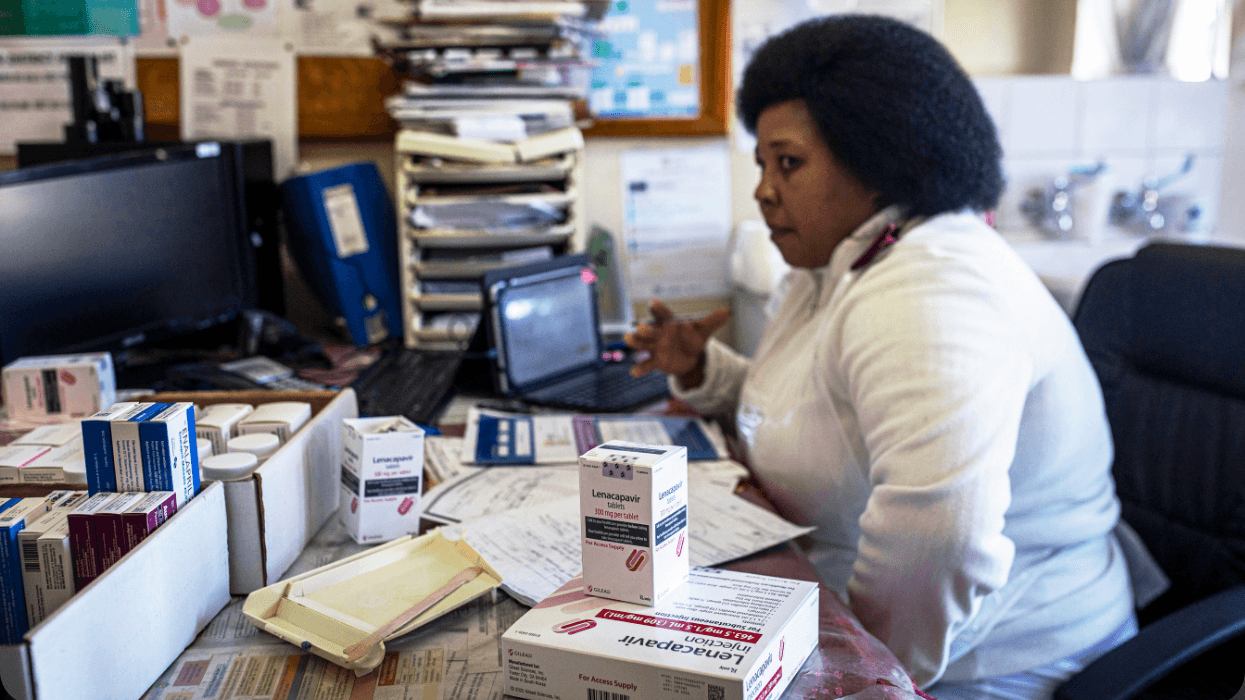 Boxes of medicines sit on a desk. A medical provider sits behind the desk.