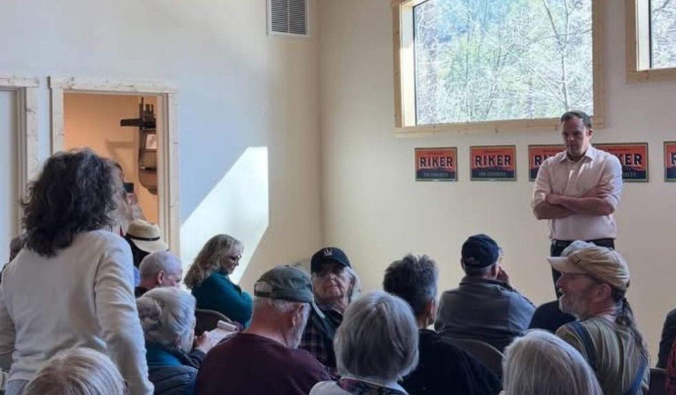 brandon riker standing before a townhall audience listening to a person speak
