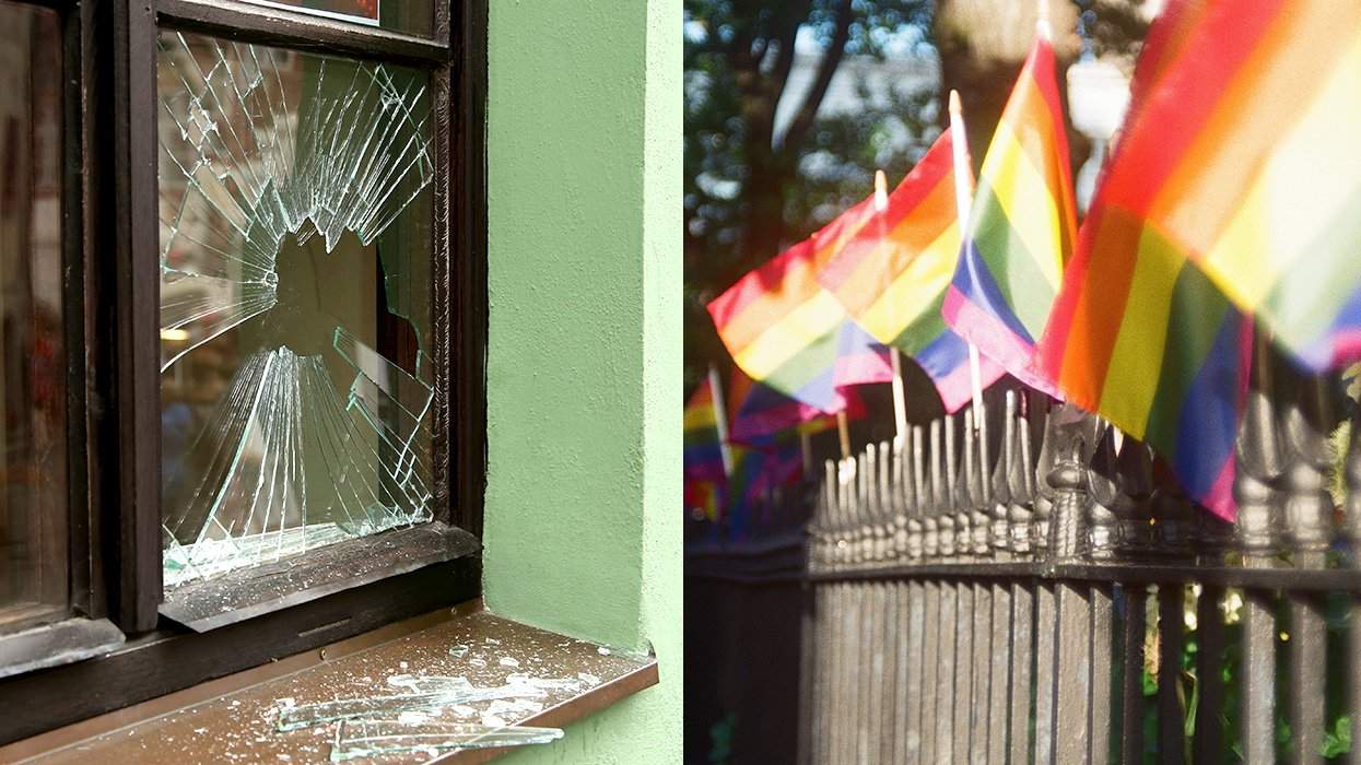 broken house window alongside rainbow LGBTQIA pride flags on a black iron fence