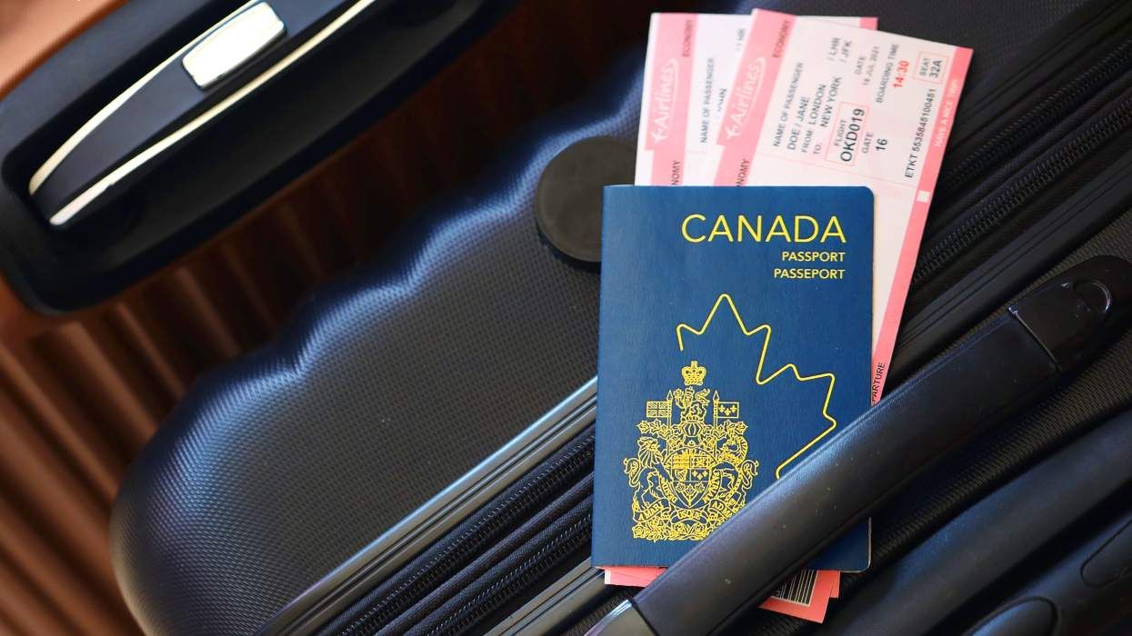 canadian passport with international travel tickets tucked into the top of luggage