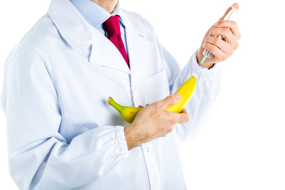 Caucasian male doctor dressed in white coat, blue shirt and red tie is making an injection to a banana