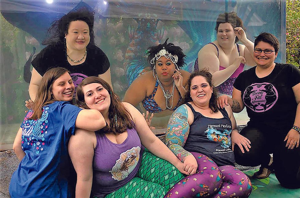 Ch\u00e8 Monique poses with members of the Society of Fat Mermaids during a group photo, with several participants wearing mermaid tails or mermaid-themed clothing.