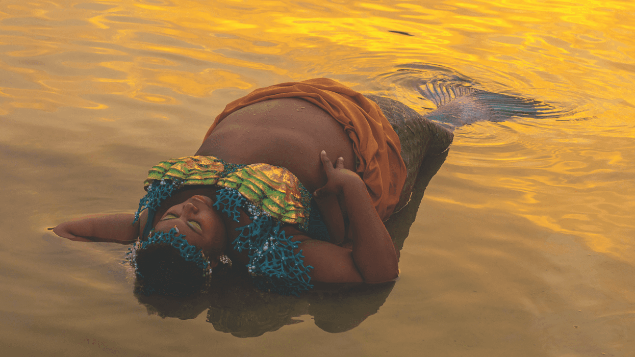 Chè Monique, wearing a mermaid tail and costume, floats on the surface of the water at sunset.