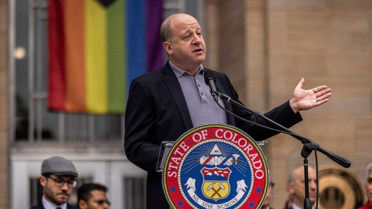 colorado gov. jared polis speaking behind the state seal and in front of an lgbtq pride flag