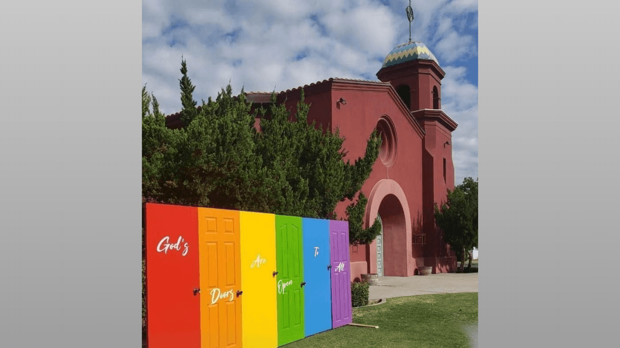 Colorful doors with "God's Doors Are Open To All" beside a red church.