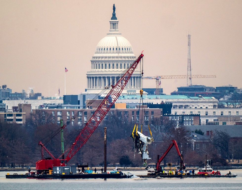 cranes pulling airplane wreckage from the Potomac River with US Capitol building behind