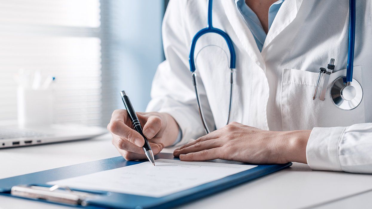 doctor in lab coat at desk writing paperwork